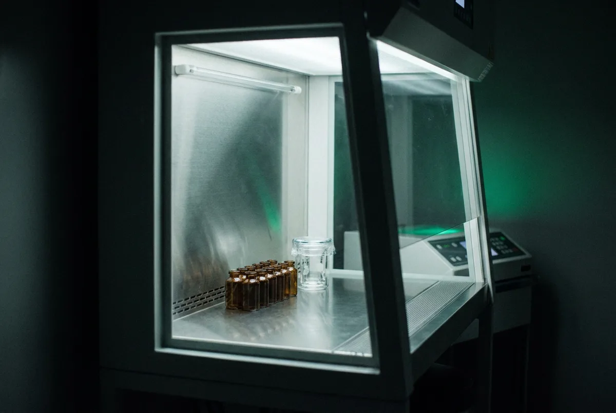 Frascos âmbar sem rótulo sobre bancada de aço inox em capela de fluxo laminar de farmácia de manipulação